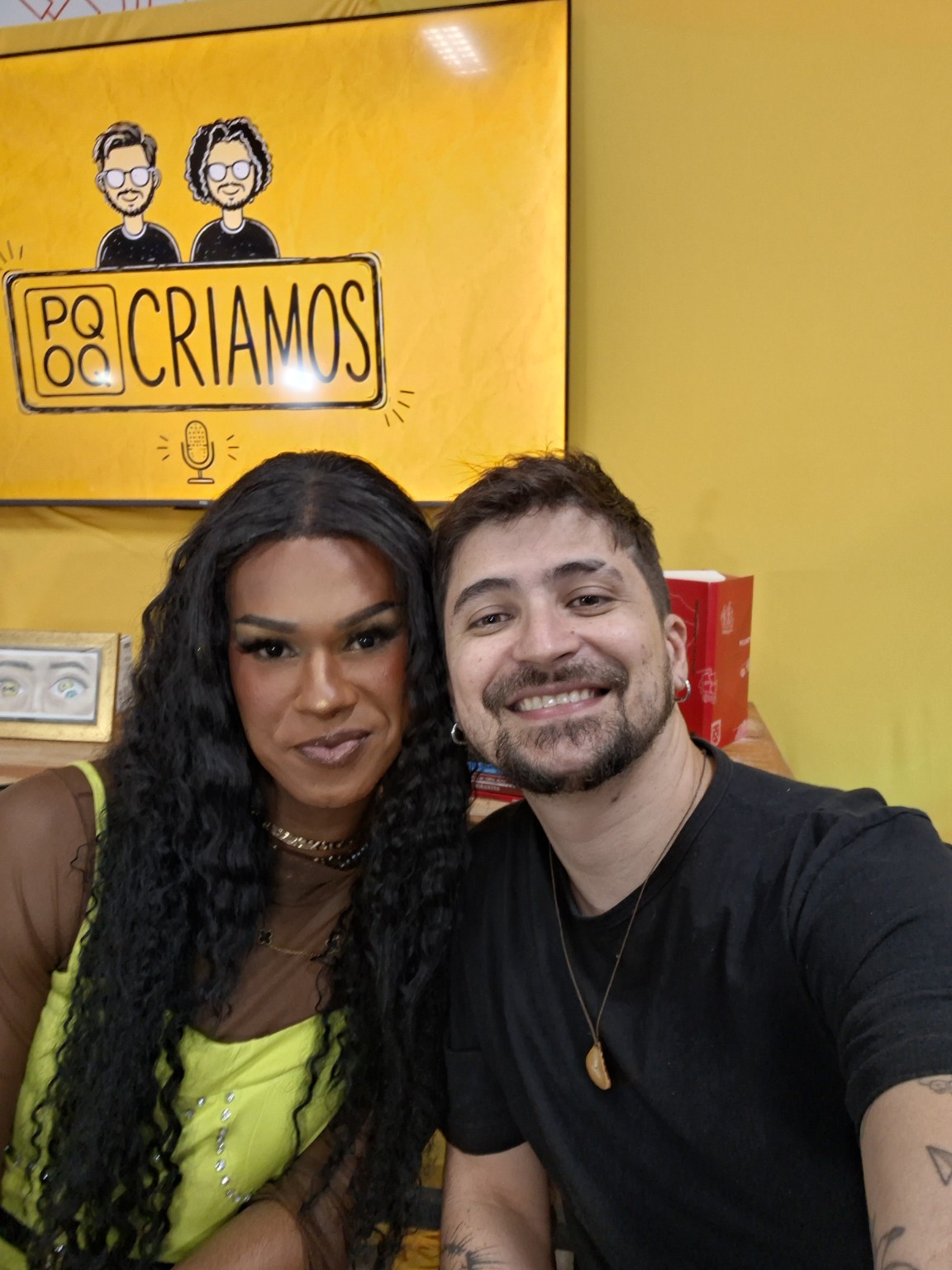 Duas pessoas diante de um painel amarelo com a marca PQOQ Criamos